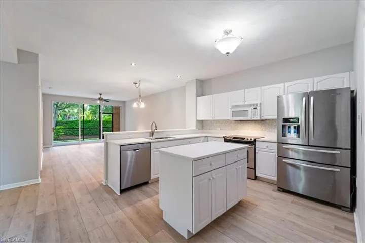 Kitchen with appliances with stainless steel finishes, a center island, white cabinets, a peninsula, and light countertops