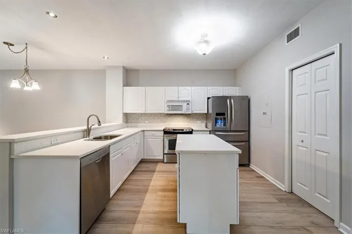 Kitchen with stainless steel appliances, light wood-type flooring, white cabinets, a kitchen island, and light countertops
