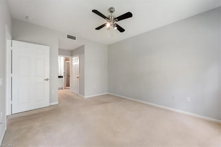 Unfurnished bedroom featuring light colored carpet, ensuite bathroom, and a ceiling fan