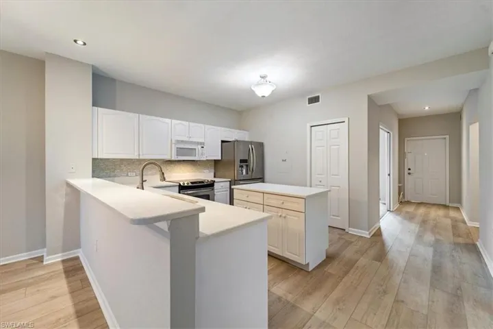 Kitchen featuring stainless steel appliances, a center island, light countertops, light wood-style floors, and backsplash