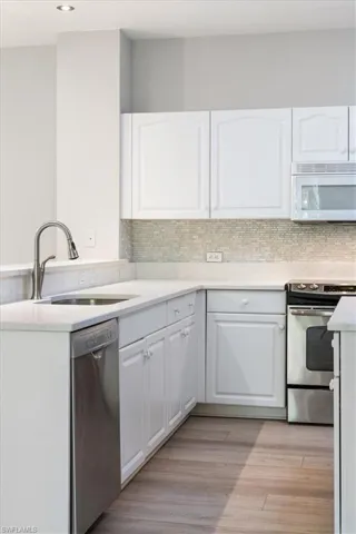 Kitchen with stainless steel appliances, white cabinets, backsplash, light countertops, and recessed lighting