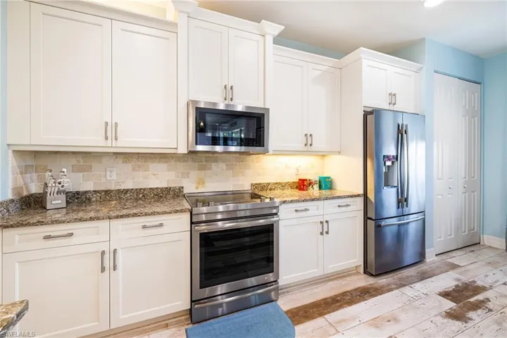 Kitchen featuring light wood finished floors, dark stone counters, stainless steel appliances, white cabinetry, and backsplash
