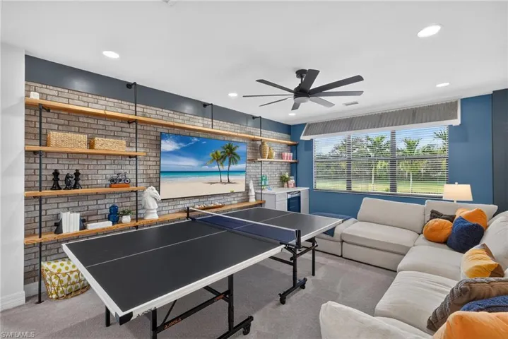 Recreational loft featuring a brick accent wall with wood shelving, large windows with blinds, a built-in wet bar, and recessed lighting