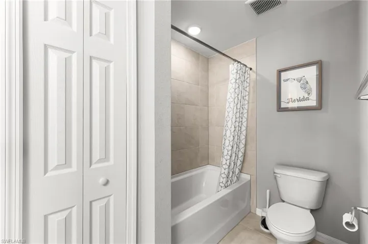 Bathroom with a closet, shower / bath combination with curtain, and tile patterned flooring