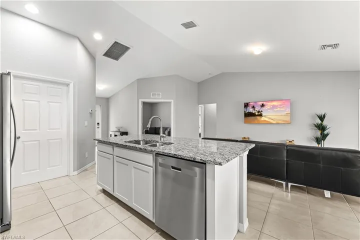Kitchen featuring stainless steel appliances, light stone countertops, open floor plan, a kitchen island with sink, and white cabinetry
