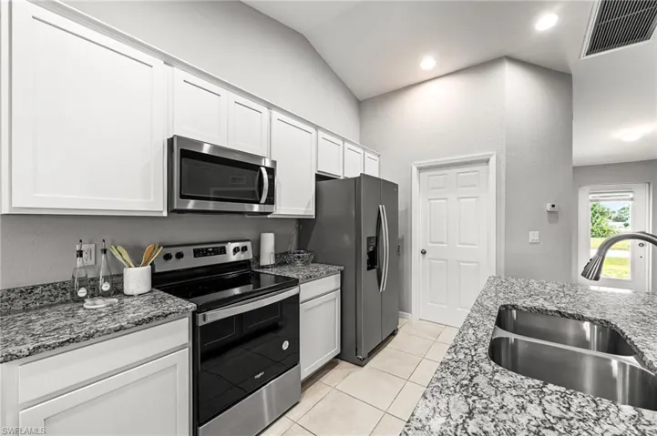 Kitchen featuring stainless steel appliances, light stone counters, light tile patterned floors, white cabinetry, and recessed lighting