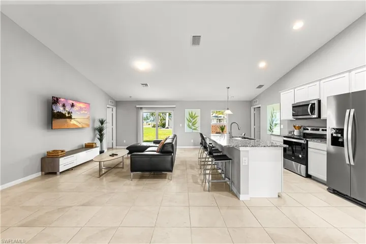 Kitchen featuring vaulted ceiling, open floor plan, appliances with stainless steel finishes, a breakfast bar area, and a kitchen island with sink