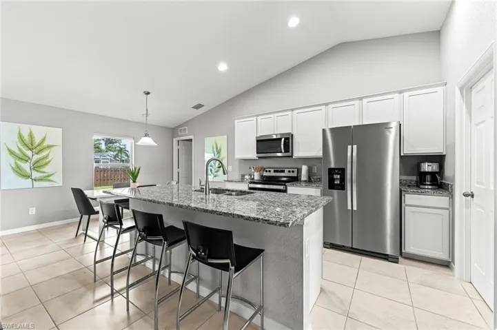 Kitchen featuring appliances with stainless steel finishes, a kitchen bar, light stone countertops, a kitchen island with sink, and white cabinetry
