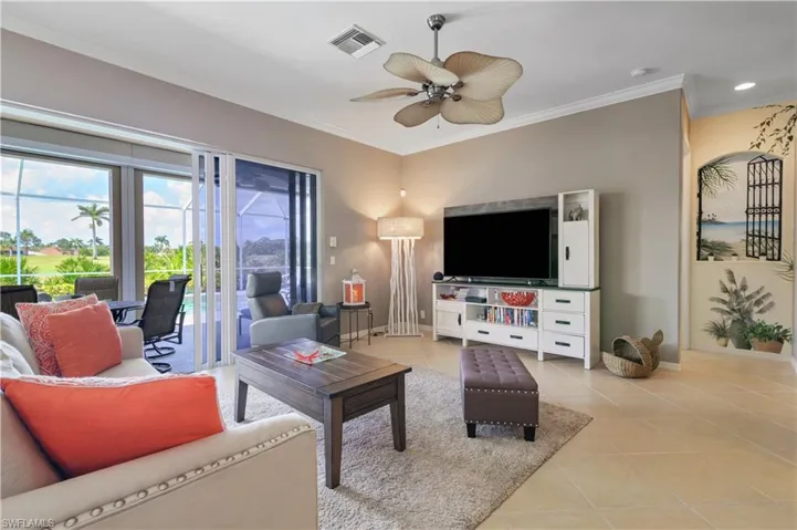 Living room with crown molding, baseboards, light tile patterned flooring, visible vents, and a ceiling fan