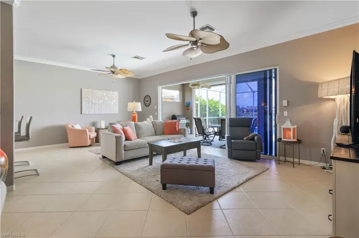 Living area with ornamental molding, baseboards, light tile patterned flooring, visible vents, and ceiling fan