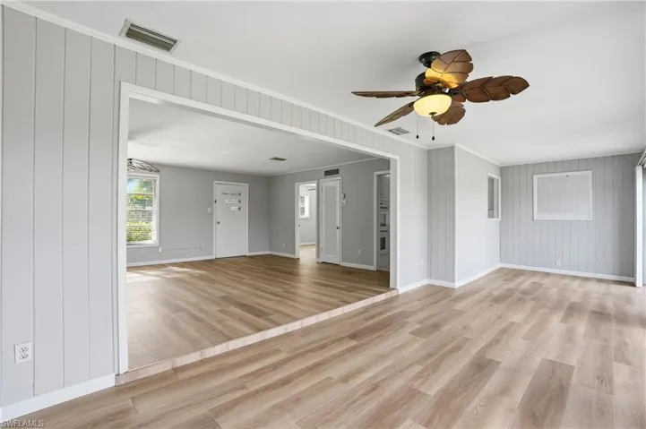 Unfurnished living room featuring light wood-style floors, ornamental molding, ceiling fan, and wood walls