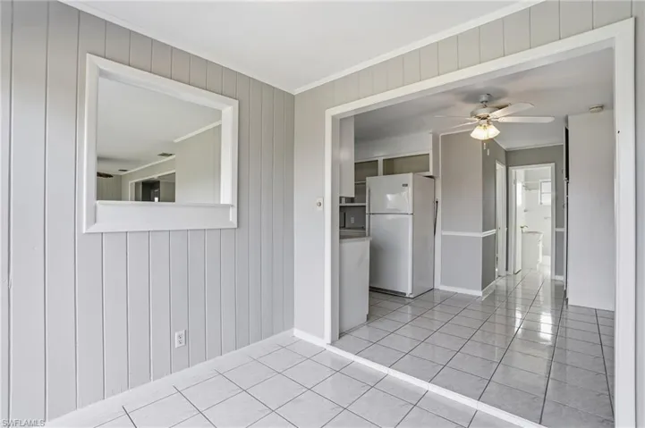 Empty room with a ceiling fan, wood walls, light tile patterned floors, and ornamental molding