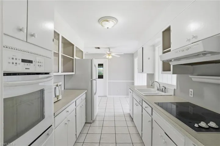 Kitchen featuring white cabinetry, white appliances, light countertops, under cabinet range hood, and light tile patterned flooring