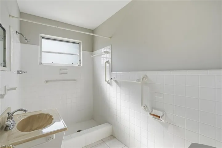 Bathroom featuring tiled shower, vanity, tile walls, wainscoting, and tile patterned flooring