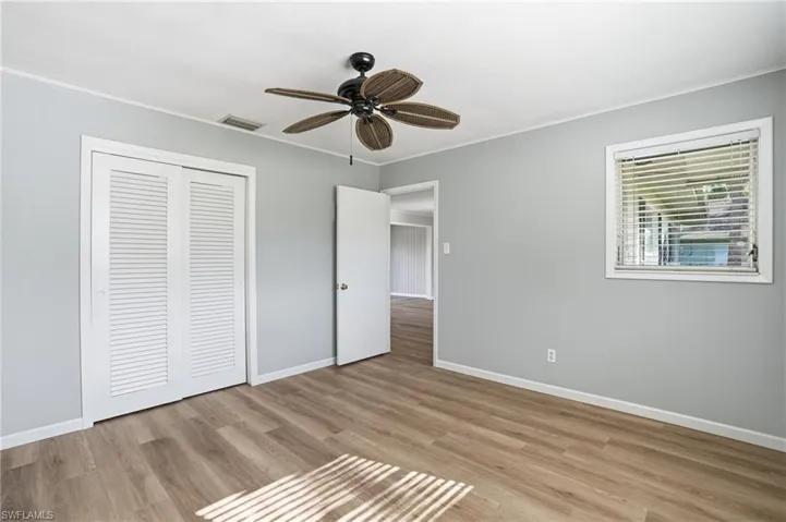 Unfurnished bedroom with light wood-style floors, a closet, a ceiling fan, wooden walls, and ornamental molding