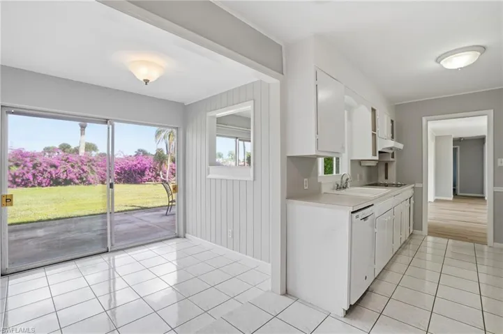 Kitchen featuring light countertops, white cabinetry, light tile patterned floors, white dishwasher, and under cabinet range hood