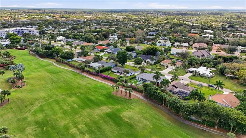 Aerial view of property and surrounding area featuring a golf course and nearby suburban area