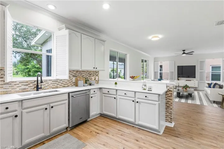 Kitchen with a peninsula, open floor plan, stainless steel dishwasher, tasteful backsplash, and light wood-style flooring