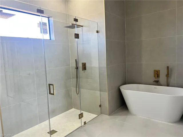 Full bathroom featuring a stall shower, a freestanding bath, tile walls, and tile patterned floors