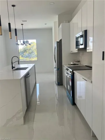 Kitchen featuring range, decorative light fixtures, modern cabinets, white microwave, and stainless steel fridge