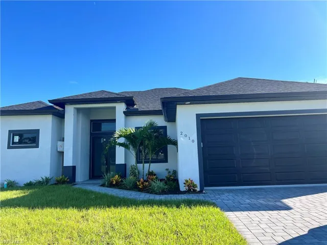 View of front of house featuring stucco siding, a front yard, driveway, roof with shingles, and a garage