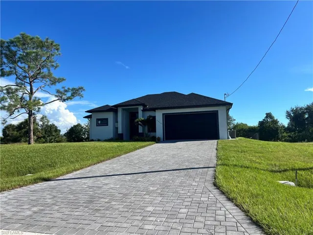 Prairie-style home with a front lawn, decorative driveway, stucco siding, and a garage