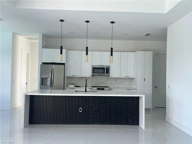 Kitchen featuring appliances with stainless steel finishes, light stone countertops, white cabinets, and pendant lighting