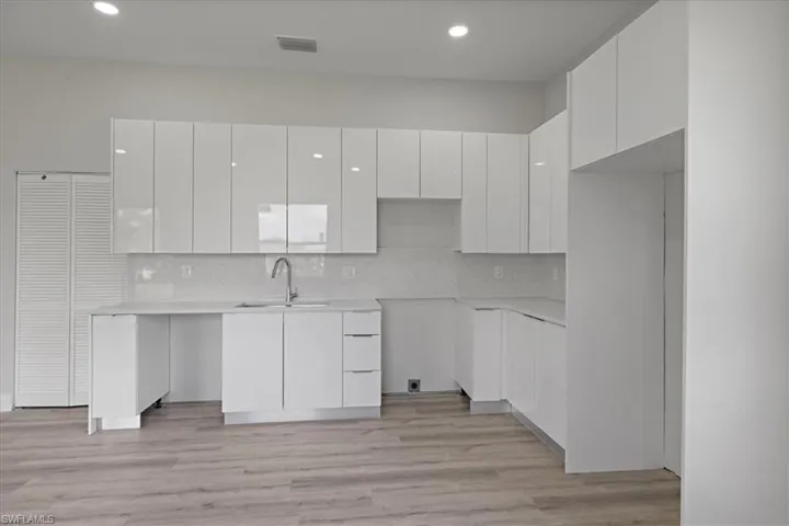 Kitchen featuring modern cabinets, white cabinets, light wood finished floors, tasteful backsplash, and recessed lighting
