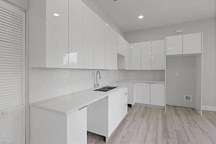 Kitchen featuring modern cabinets, white cabinets, backsplash, light stone counters, and light wood finished floors