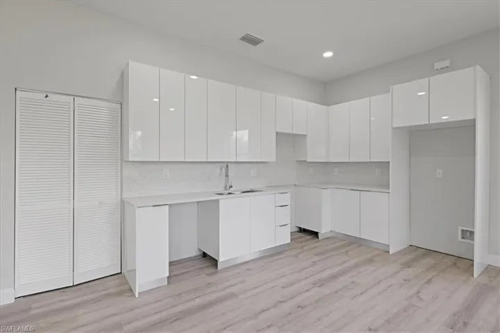 Kitchen with modern cabinets, white cabinetry, decorative backsplash, light wood finished floors, and recessed lighting