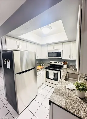 Kitchen featuring appliances with stainless steel finishes, white cabinets, a raised ceiling, light stone counters, and light tile patterned floors