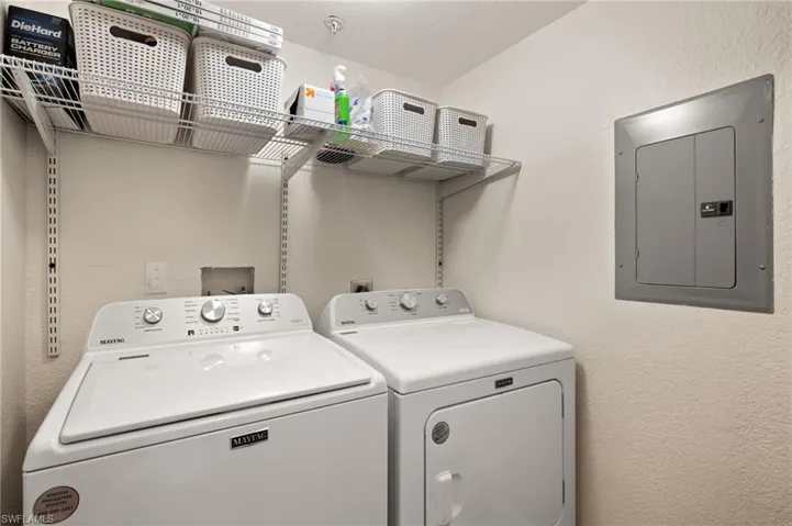 Laundry area with a textured wall, electric panel, and washing machine and clothes dryer