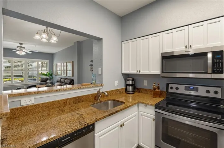 Kitchen with appliances with stainless steel finishes, light stone counters, white cabinetry, open floor plan, and a chandelier