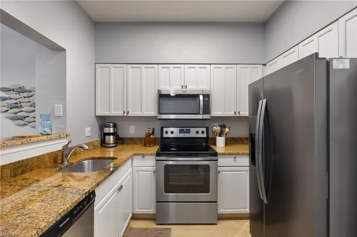 Kitchen with appliances with stainless steel finishes, white cabinets, light stone counters, and a textured wall