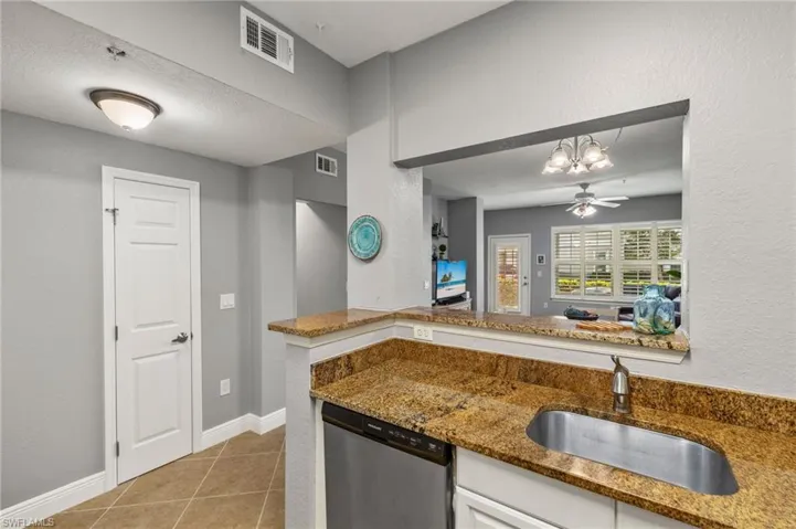 Kitchen with a textured wall, light tile patterned floors, stainless steel dishwasher, light stone countertops, and white cabinets