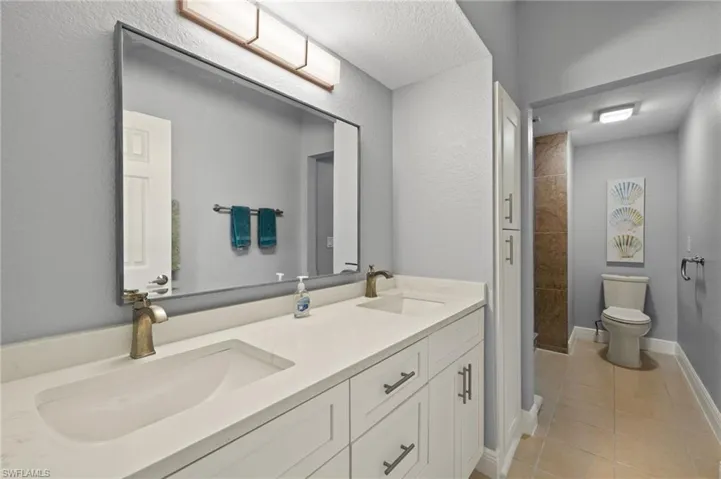 Full bathroom featuring a textured wall, double vanity, light tile patterned floors, and tiled shower