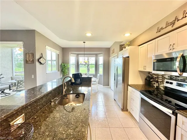 Kitchen featuring sink, dark stone countertops, stainless steel appliances, white cabinets, and decorative light fixtures