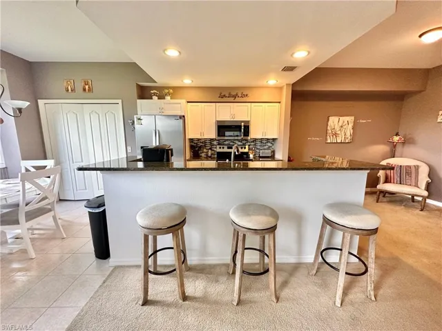 Kitchen with dark stone countertops, stainless steel appliances, a breakfast bar, and white cabinets