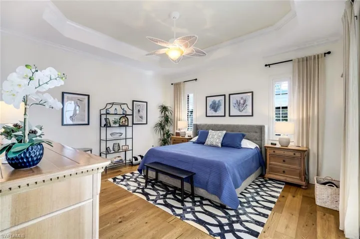 Primary bedroom with wood flooring,  tray ceiling, and crown molding