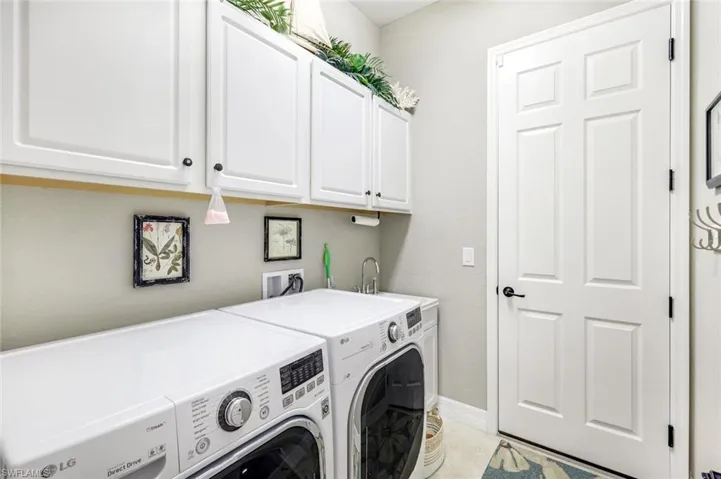 Clothes washing area featuring separate washer and dryer, light tile patterned flooring, cabinet space, and baseboards