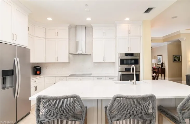 Kitchen with stainless steel appliances, backsplash, light stone counters, wall chimney range hood, and recessed lighting