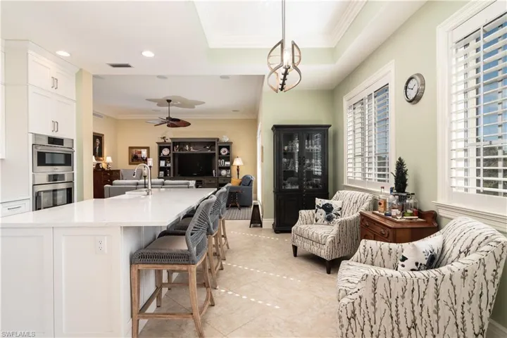 Kitchen with open floor plan, white cabinetry, decorative light fixtures, ornamental molding, and a breakfast bar area