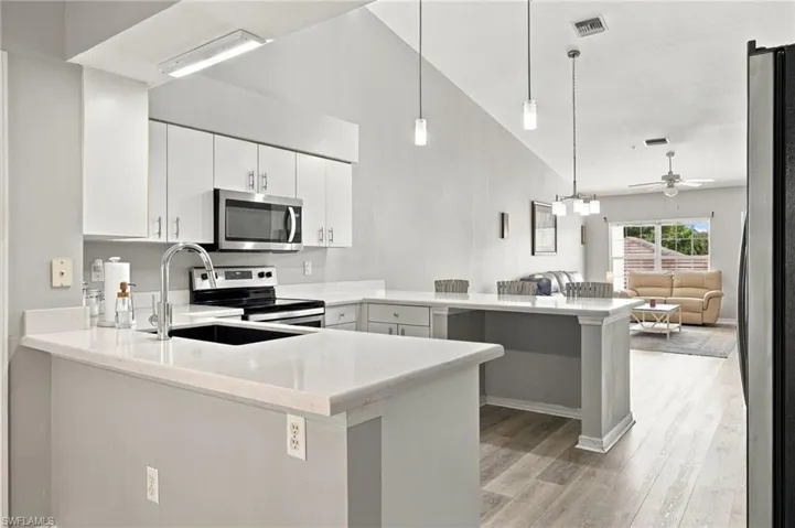 Kitchen featuring white cabinetry, stainless steel appliances, a black undermount sink, and light-toned countertops
