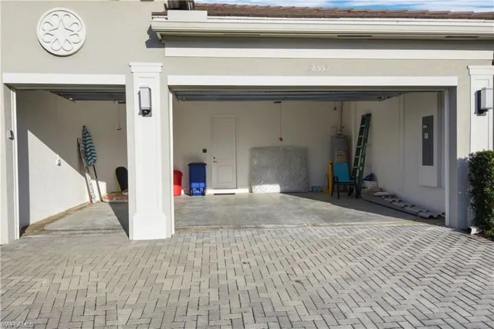 Garage featuring decorative driveway, electric panel, and water heater
