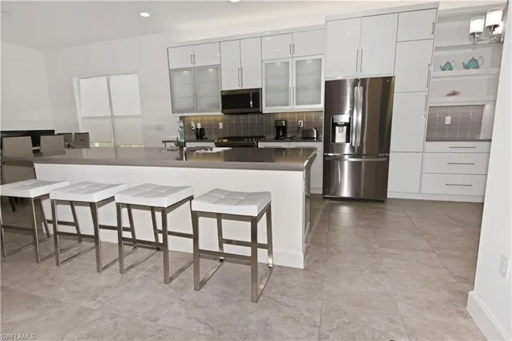 Kitchen featuring stainless steel appliances, white cabinets, a kitchen breakfast bar, dark countertops, and glass fronted cabinets