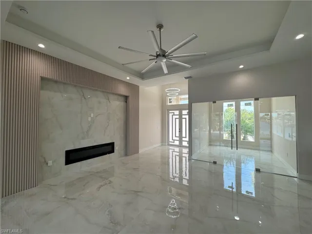 Unfurnished living room with a fireplace, french doors, a tray ceiling, and ceiling fan