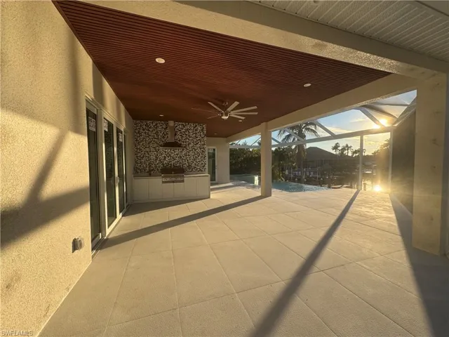 Patio terrace at dusk with area for grilling, ceiling fan, and glass enclosure