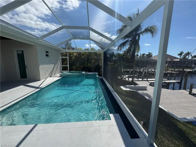 View of pool with an in ground hot tub, a dock, glass enclosure, and a patio