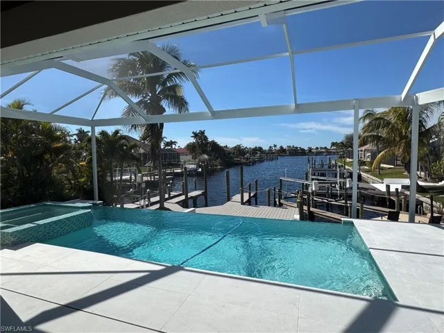 View of pool with a patio, glass enclosure, a water view, a boat dock, and an in ground hot tub