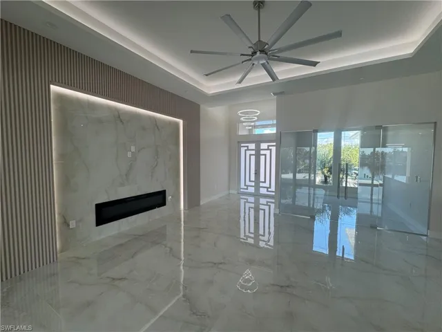 Unfurnished living room featuring a raised ceiling, ceiling fan, and a fireplace